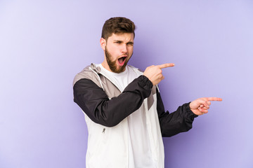 Young man isolated on purple background pointing with forefingers to a copy space, expressing excitement and desire.