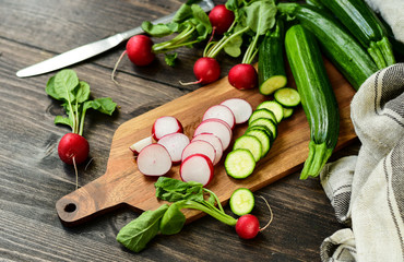 radishes and zucchini sliced on a wooden board. salad with fresh seasonal vegetables. diet food....