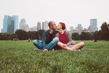 Happy couple enjoying romantic vacation outdoors in Central Park, New York City, USA. Smiling tourists man and woman in summer sun sitting on grass in Manhattan. Dating young couple happy in love.