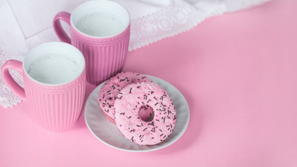 pink milk cups and doughnuts with pink frosting in a plate on a pink background top view. the milk in the cups and the cakes lay flat. milk ceramic cups and copy space.