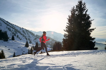 Trail runner in pink jacket woman running in winter mountains trail on snow.