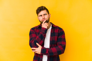 Fototapeta premium Young caucasian man isolated on yellow background looking sideways with doubtful and skeptical expression.