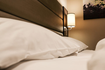 Fresh bedding seen on a luxury kings' sized bedroom in a premium-grade hotel. The modern lighting...