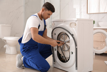 Professional plumber repairing washing machine in bathroom