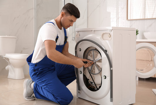 Professional plumber repairing washing machine in bathroom