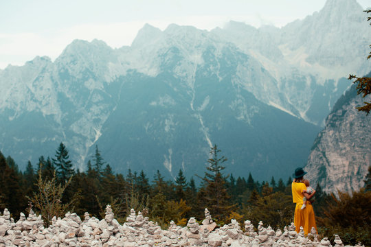 Back of mother outside in nature hugging her baby in front of a  big mountain with stone sculptures, looking out at beautiful panoramic view