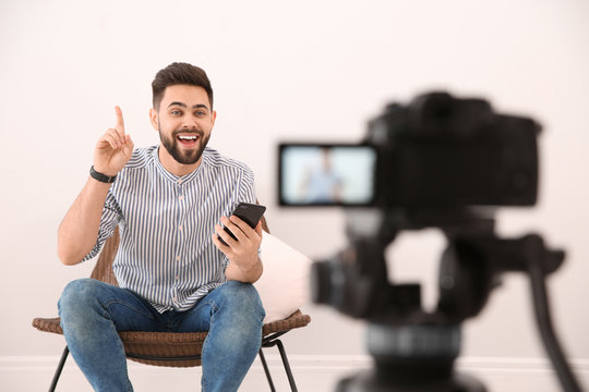 Young blogger with smartphone recording video on camera indoors
