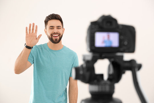 Young blogger recording video on camera against white background