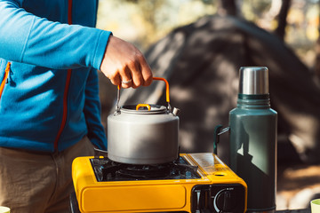 Hand lighting fire at campsite plate for cooking, making tea or coffee. Outdoor food drink item set. Travel tools, camping equipment. Nature picnic rest. Campfire kettle, thermos with hot beverage.