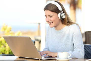 Happy student e-learning with headphones and laptop in a cafe
