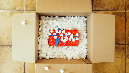 Red present box in big shipping box. Opening a parcel contains a gift. Unpacking box with another box. Surprise. People, delivery, shipping service, opening cardboard box or parcel at home.