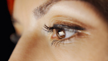 Close-up of beautiful young woman eyes looking at monitor, working with computer, laptop. Monitor light is reflected in brown eyes. Evening woman freelancer working, read books, watch video online.