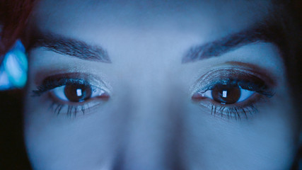 Close-up of beautiful woman eyes looking at monitor, working from home with computer, laptop. Screen blue light is reflected in her eyes. Woman freelancer working, shopping online, watch video.
