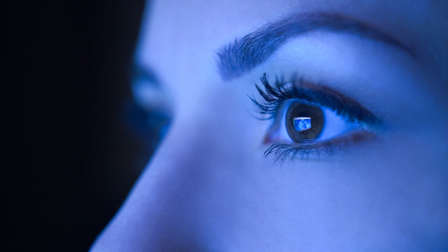 Close-up of beautiful woman eyes looking at monitor, working from home with computer, laptop. Screen blue light is reflected in her eyes. Woman freelancer working, shopping online, watch video.