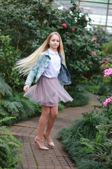 Young girl with long white hair in a denim jacket walks in the garden with blooming azalea