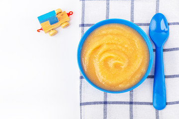 Baby food. Fresh homemade applesauce. Blue bowl with fruit puree on fabric and kids toys on table. The concept of proper nutrition and healthy eating. Organic and vegetarian food. Copy space for text