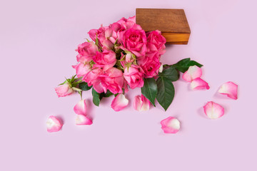 Fresh pink roses in a wooden box on a pink background. Flying rose petals. View from above.