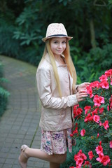 Young girl with long blond hair in a powdery jacket and a hat enjoys in the garden with blooming azalea