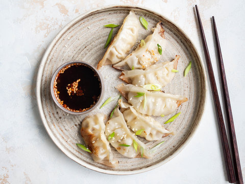 Chinese traditional dumplings - gyoza with pork and vegetables on a round plate with soy sauce in a bowl. Top view.