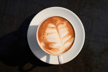classic coffee cup in vintage white color with palm leaf shape latte art coffee isolated on black granite stone table top view