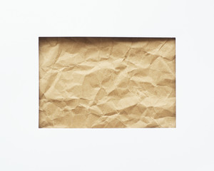 A rectangular hole in a white sheet of paper. Crumpled craft paper in the background. Space for copy...