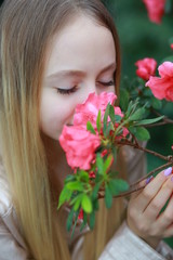 Fototapeta premium Young girl with long blond hair in a powdery jacket enjoys in the garden with blooming azalea