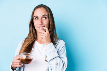 Young caucasian woman holding a tea isolated relaxed thinking about something looking at a copy space.