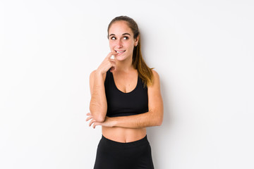 Fototapeta na wymiar Young caucasian fitness woman posing in a white background relaxed thinking about something looking at a copy space.
