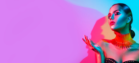 Portrait de femme modèle haute couture dans des néons lumineux colorés, belle fêtarde avec maquillage tendance, manucure, coiffure. Pointant la main, geste publicitaire sur fond vif coloré