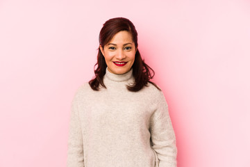 Middle age latin woman isolated on a pink background happy, smiling and cheerful.