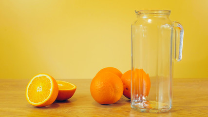Freshly squeezed orange juice in glass jar on yellow colorful background. Pouring orange juice into the glass pitcher. Orange juice, healthy, organic drink. Glass of orange juice and orange slices.