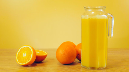 Freshly squeezed orange juice in glass jar on yellow colorful background. Pouring orange juice into the glass pitcher. Orange juice, healthy, organic drink. Glass of orange juice and orange slices.