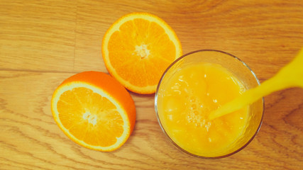 Freshly squeezed orange juice in glass, close-up. Pouring orange juice into the glass on wooden background. Orange juice, healthy, organic drink. Glass of orange juice and orange slices. Top view.