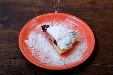 A piece of berry pie dusted with powdered sugar in the plate and a spoon. Close up photo of cake slice. Beautiful and sweet bakery.