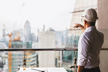 Portrait engineer man wearing safety helmet standing back and looking to the construction site with...