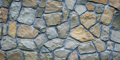 Gray stone wall. Texture of grey granite. Uneven rock surface of floor, decorative tile of facade building. Wide panorama. Mosaic pattern of stones, cement.