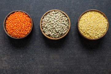 Red, green and yellow lentils in wooden bowl on grey rustic background, uncooked various dried lentil legumes