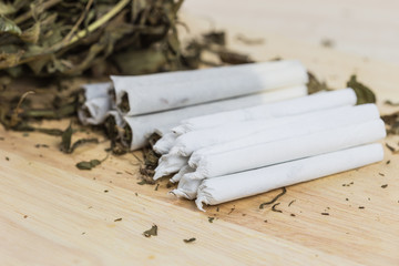 Close up shot of cannabis joints on wooden background and on the white paper ready to be rolled.