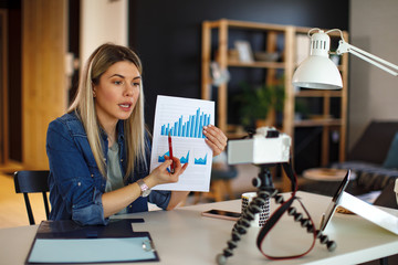 Young business woman recording video for her vlog shows papers with graphs