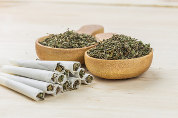 Joint of marijuana. Spoon filled with weed, grinder and wooden background. Rolling a joint and smoking weed.