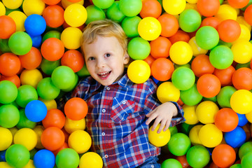 Fototapeta na wymiar Happy child, kid boy playing, having fun on playground with colorful plastic balls in pool. Game center for family weekend, holiday party with kids, games area room. Entertainment center with toys.