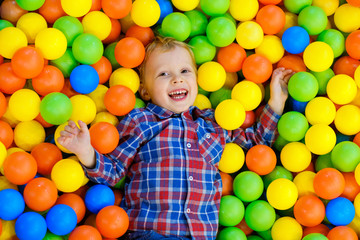 Fototapeta na wymiar Happy child, kid boy playing, having fun on playground with colorful plastic balls in pool. Game center for family weekend, holiday party with kids, games area room. Entertainment center with toys.