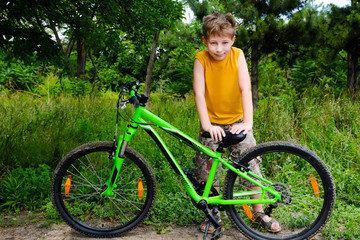 Fototapeta na wymiar Cute active little boy riding on bike on warm summer day at countryside. Active leisure and sports for kids. Portrait of child, kid with green bicycle looking at camera. Sport, health and fun.