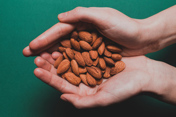 Top view on hands holding almonds on a green background