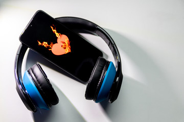 Blauer Funkkopfhörer mit schwarzem Smartphone und brennendem Herz zeigt die feurige Liebe zur...