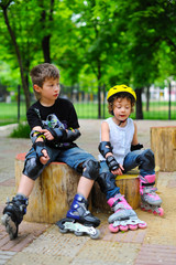Little girl and boy, friends in roller skates in park at summer. Pretty children, kids, brother and sister riding a roller, wearing roller skates and protective equipment.