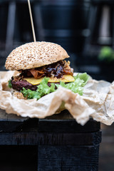 Burger owinięty w papier ekologiczny w tle industrialny styl, czarne tło. Hamburger z mięsem ze świeżymi dodatkami w bułce sezamowej.  - obrazy, fototapety, plakaty