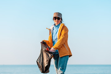 A young Caucasian woman in a jacket collects garbage and puts it in a plastic bag. In the...