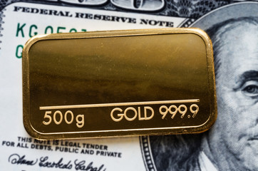 Gold bar weighing 500 grams 999.9, fineness against a blurred background of dollar bills.