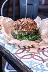 Świeżo grillowany burger leży na stoliku azelejos. Kanapka w amerykańskim stylu zawinięta w papier ekologiczn, street food. Restauracja w industrialnym stylu.  - obrazy, fototapety, plakaty